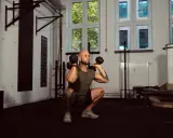 Mann macht Kniebeugen mit Kurzhanteln. Ein Supersatz ist, wenn zwei Übungen direkt hintereinander ohne Pause ausgeführt werden.