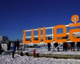 Stor orange skylt med texten "LULEÅ" i snöig miljö. Perfekt för luleå travel, en solig vinterdag.
