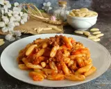 Un piatto invitante di malloreddus alla campidanese, conditi con un ricco ragù di carne. Sullo sfondo, fiori bianchi e un ciotola di pasta cruda.