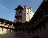 Zamek w Korzkwi z drewnianymi gankami i wieżą, na której powiewa polska flaga.