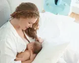Matka karmi piersią swoje 6 miesięczne dziecko w łóżku.