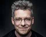 Uśmiechnięty mężczyzna w okularach, z siwymi, nastroszonymi włosami. Może to być jeden z bohaterów Felix Net i Nika, gotowy na przygodę.
