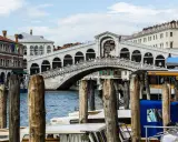 Le célèbre pont du Rialto à Venise, animé par des touristes, surplombe le Grand Canal où naviguent des gondoles et des taxis nautiques.