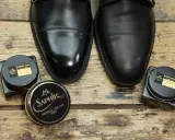Czarne, eleganckie buty i dwa słoiczki Saphir: krem do skóry i olejek. Idealne, by dowiedzieć się, czym natłuścić skórzane buty.
