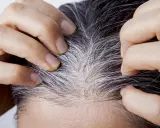 Manos separando cabello oscuro con canas plateadas, buscando cómo cubrir canas sin tinte.