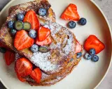 En hög med gyllene french toast, toppad med färska jordgubbar, blåbär och pudersocker. Ett perfekt recept för en lyxig frukost.