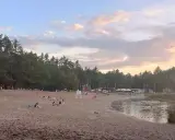 Plaża nad jeziorem w Jelczu Laskowicach, ludzie odpoczywają, dzieci bawią się na dmuchanym zjeżdżalni, a niektórzy kąpią się w wodzie.