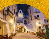 Un vicolo illuminato ad Atrani, con un arco giallo in primo piano e un campanile con orologio sullo sfondo.