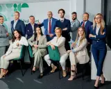 Grupa profesjonalistów w garniturach pozuje do zdjęcia w nowoczesnym biurze.
