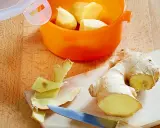 Frische Ingwerstücke werden geschält und in einem orangen Behälter aufbewahrt, um **Ingwer haltbar zu machen**. Ein Messer liegt daneben.