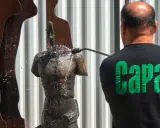 Hombre con camiseta negra "Capa" limpia una estatua de bronce con agua a presión.