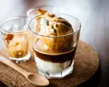 Ein italienischer Eiskaffee, Affogato, mit Vanilleeis und heißem Espresso. Ein Holzlöffel liegt daneben.