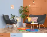 Nowoczesny salon z szarymi fotelami i kanapą, akcentem jest ściana w kolorze oranżowym.