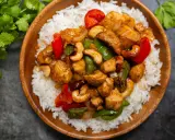 Un délicieux poulet noix de cajou servi sur un lit de riz blanc. Des poivrons rouges et verts ajoutent de la couleur à ce plat savoureux.