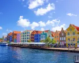 Färgstarka hus längs en kaj, en båt i vattnet. Här kan man se var ligger Curacao, en karibisk pärla.