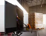 Un operario usa una carretilla para el transporte de materiales, cargando cajas en un camión.