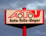 Schild mit rotem Schriftzug "A.T.U. Auto-Teile-Unger" vor bewölktem Himmel.