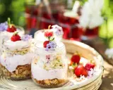 En härlig sommardessert i glasburkar, en himmelsk jordgubbstårta med fluffig grädde och saftiga jordgubbar, dekorerad med små lila blommor.