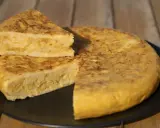 Una deliciosa tortilla de patatas, con una porción cortada y apilada, servida en un plato negro sobre una mesa de madera.
