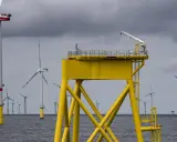 Große gelbe Plattform mit Kran inmitten vieler Windkraftanlagen im Meer. Die Zukunft der Windkraft onshore und offshore.