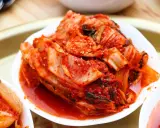 Kilka białych miseczek z pikantnym, czerwonym kimchi na drewnianym tle.