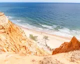 Orange cliffs overlook a sandy portugal strand algarve. Gentle waves lap the shore where a few people stroll.