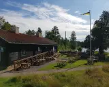 Mysigt tiveden boende med uteservering vid vattnet. En svensk flagga vajar i vinden.