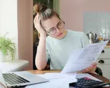 Zmartwiona kobieta analizuje dokumenty, szukając informacji o zwrocie OC po sprzedaży samochodu.