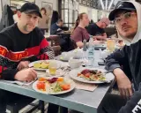 Dwóch mężczyzn, jeden w bluzie z napisem "Givenchy", drugi w bluzie "Supreme", siedzi przy stole w restauracji. Wyglądają jak bary raperzy, którzy wybrali się na wspólny posiłek.