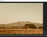 Paisaje rural con granero y montañas, con un filtro sepia aplicado en Photoshop para un estilo vintage.