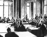 Männer in Anzügen sitzen an langen Tischen in einem prunkvollen Saal. Dies ist die Unterzeichnung des Versailler Vertrags, der den Ersten Weltkrieg beendete.