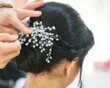 Manos expertas ajustan un tocado de perlas y cristales a un juvenil recogido de boda, creando un look elegante y romántico.