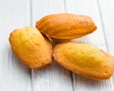 Trois délicieuses pâtés à madeleine dorées sur une planche en bois blanc.