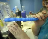 Person nutzt ein Spirometer für einen Lungenfunktionstest. Der Asthmaspray ist nicht sichtbar, aber das Gerät hilft bei der Diagnose.