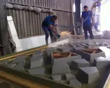 Dos operarios trabajan con material GRC en un taller, uno rocía con una manguera y el otro supervisa.