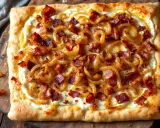 Flammekueche prête à déguster, garnie d'oignons caramélisés et de lardons croustillants sur une pâte fine et dorée. Un délice !