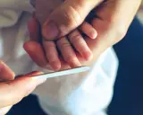 Mani adulte limano delicatamente le unghie di un neonato, un momento di cura che mostra quando si possono tagliare le unghie ai neonati.