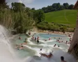 Persone si rilassano nelle cascate naturali delle **Terme di Saturnia**, immerse nel verde della campagna toscana.