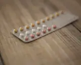 Opakowanie tabletek antykoncepcyjnych z różowymi, białymi i żółtymi pigułkami na drewnianym tle.