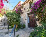 Escaleras de piedra adornadas con buganvillas y flores blancas, que llevan a la entrada de una casa de piedra. Un ejemplo de los pueblos bonitos de Alicante.