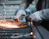Pracownik w rękawicach szlifuje metal, sypią się iskry. Wypadek przy pracy? Protokół powypadkowy wymaga dokumentacji.
