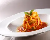 Un nido di spaghetti conditi con una salsa rossa vibrante di pomodorini freschi, guarnito con foglie di basilico verde brillante, servito in un piatto bianco elegante.
