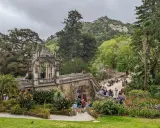 Ein märchenhafter Sintra Garten mit einer steinernen Brücke, üppiger Vegetation und Besuchern, die die Aussicht genießen.