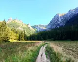 Ścieżka wije się przez dolinę małej łąki, otoczoną lasem i skalistymi szczytami.