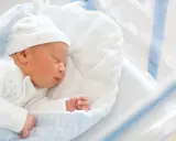 Śpiący noworodek w szpitalnym łóżeczku. Do wniosku o becikowe potrzebne są dokumenty potwierdzające urodzenie dziecka.