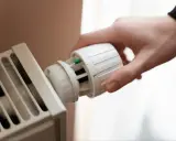 Dłoń kręci termostatem grzejnika. Kaloryfer nie grzeje, a nie jest zapowietrzony, co frustruje domowników.