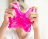 Dziecko bawi się różowym slime, który wygląda jak z przepisu na domowy slime.