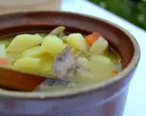 Gęsta zupa z ziemniakami, marchewką i kawałkami mięsa, być może z barania głowa, w glinianym naczyniu.