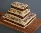 Trois parts de napolitain sans gluten empilées sur une planche en bois, garnies de vermicelles au chocolat.