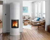 Un élégant poêle de masse blanc diffuse une douce chaleur dans un salon lumineux aux planchers de bois.